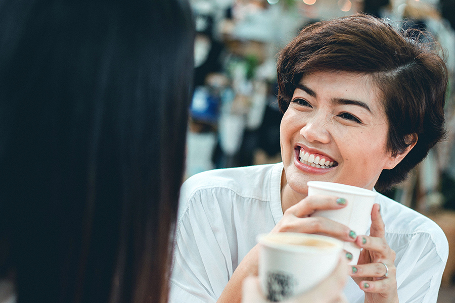 Person smiling and holding coffee cup while talking to someone.