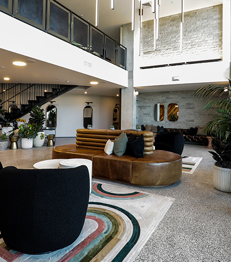 Lobby with round leather couch, plush seats, geometric rugs, and large potted plants.